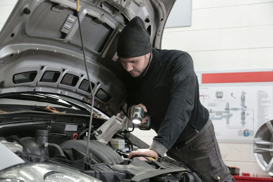 A person kneeling next to a car uses a tire iron to loosen the lug nuts on a wheel, with a toolbox nearby.