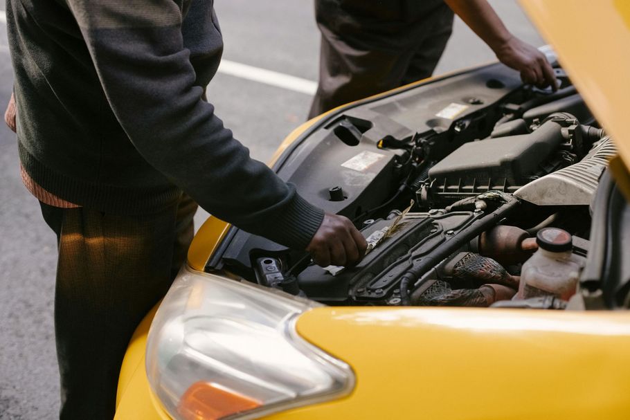 Two people standing by an open hood, inspecting the engine of a yellow car.
