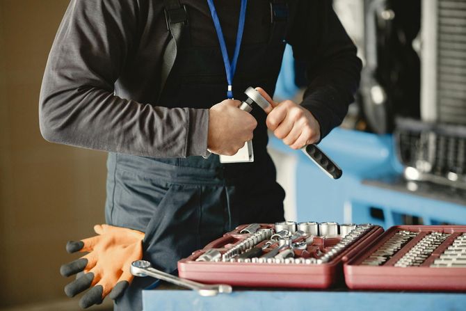 A technician in dark workwear holds a ratchet over an open tool case filled with various chrome sockets and wrenches.