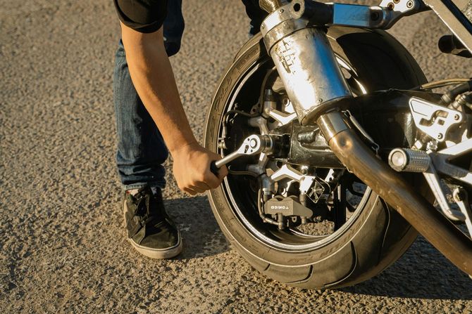 A person uses a ratchet wrench to loosen or tighten the axle nut on the rear wheel of a motorcycle outdoors.