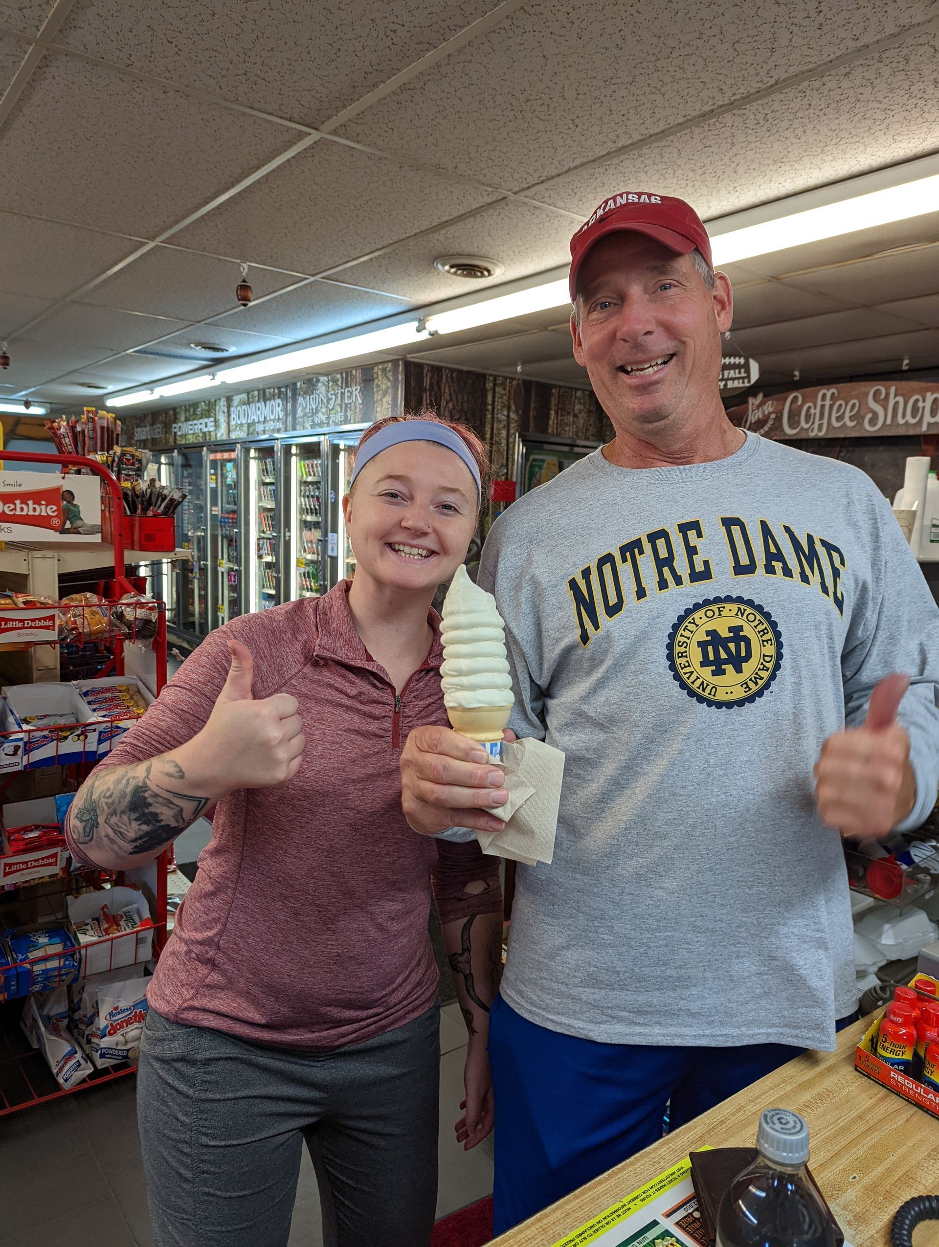 A man and a woman are standing next to each other holding ice cream cones and giving a thumbs up.