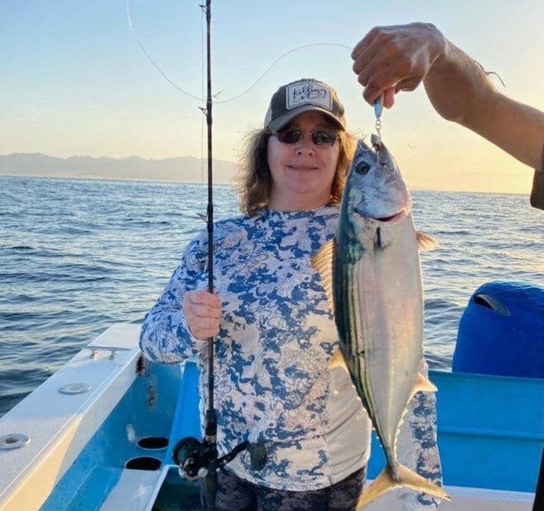 A woman is holding a fish on a boat with a fishing rod