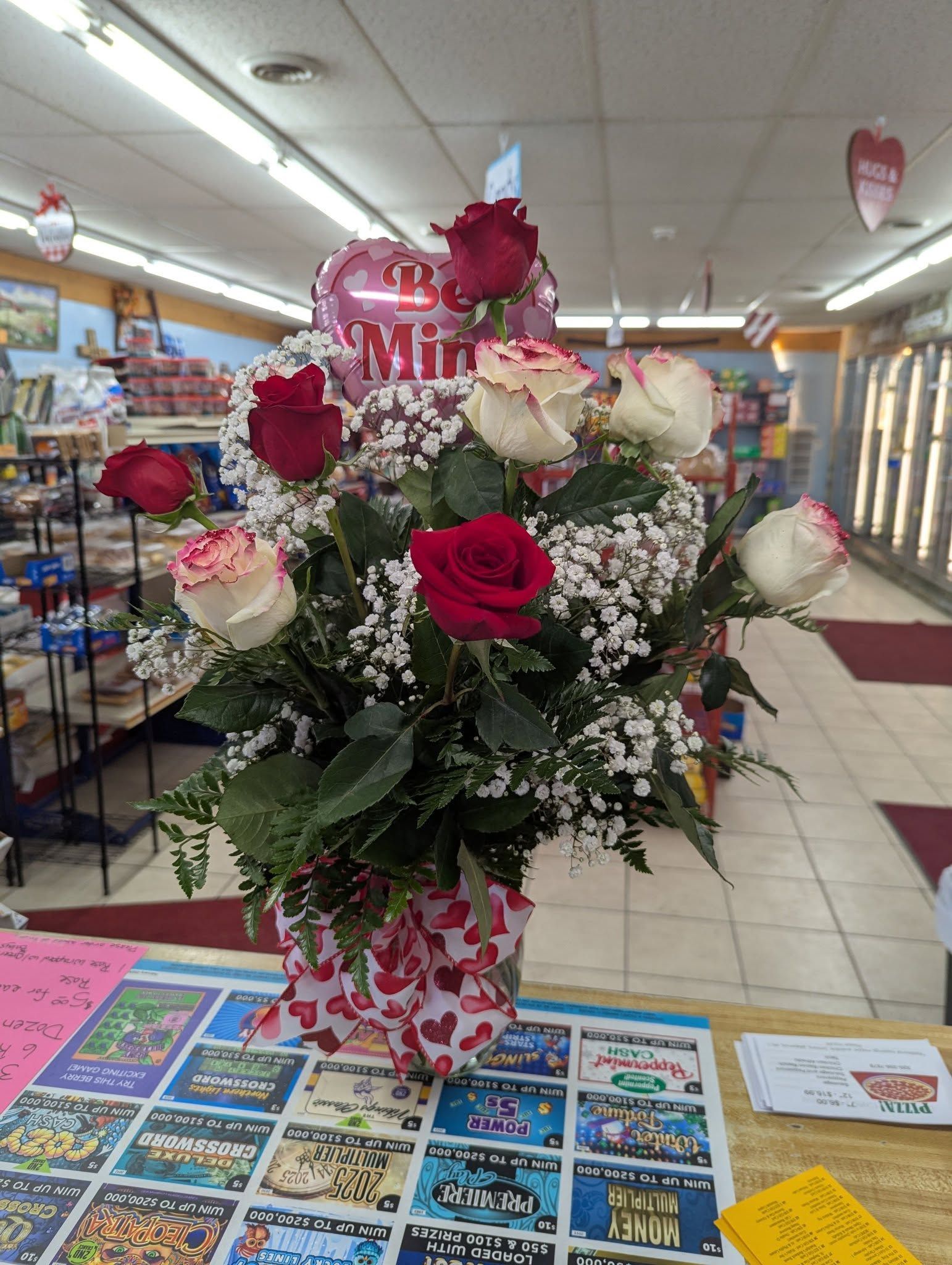 A vase filled with red and white roses and a balloon in a store.