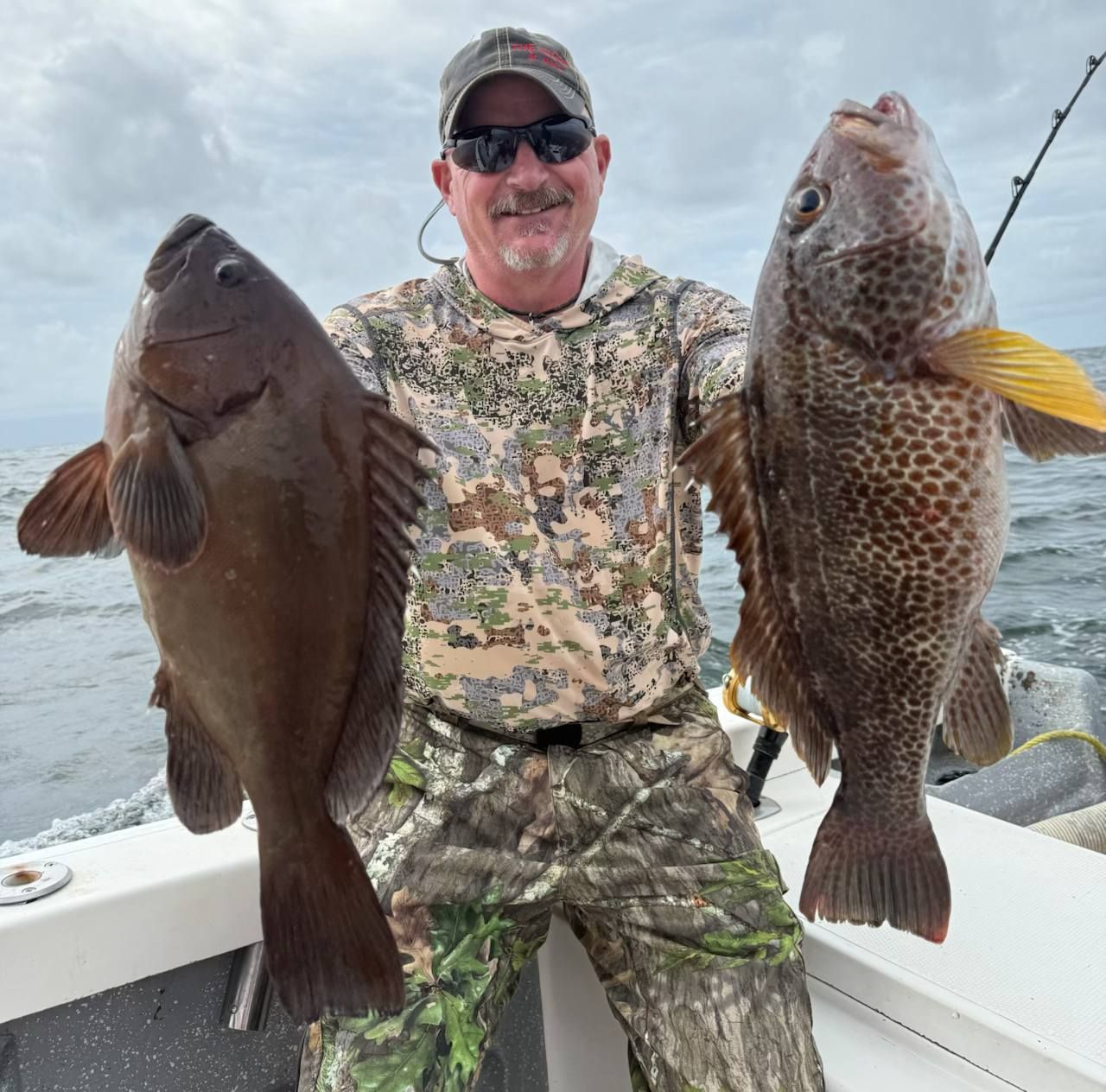A man is holding two large fish on a boat