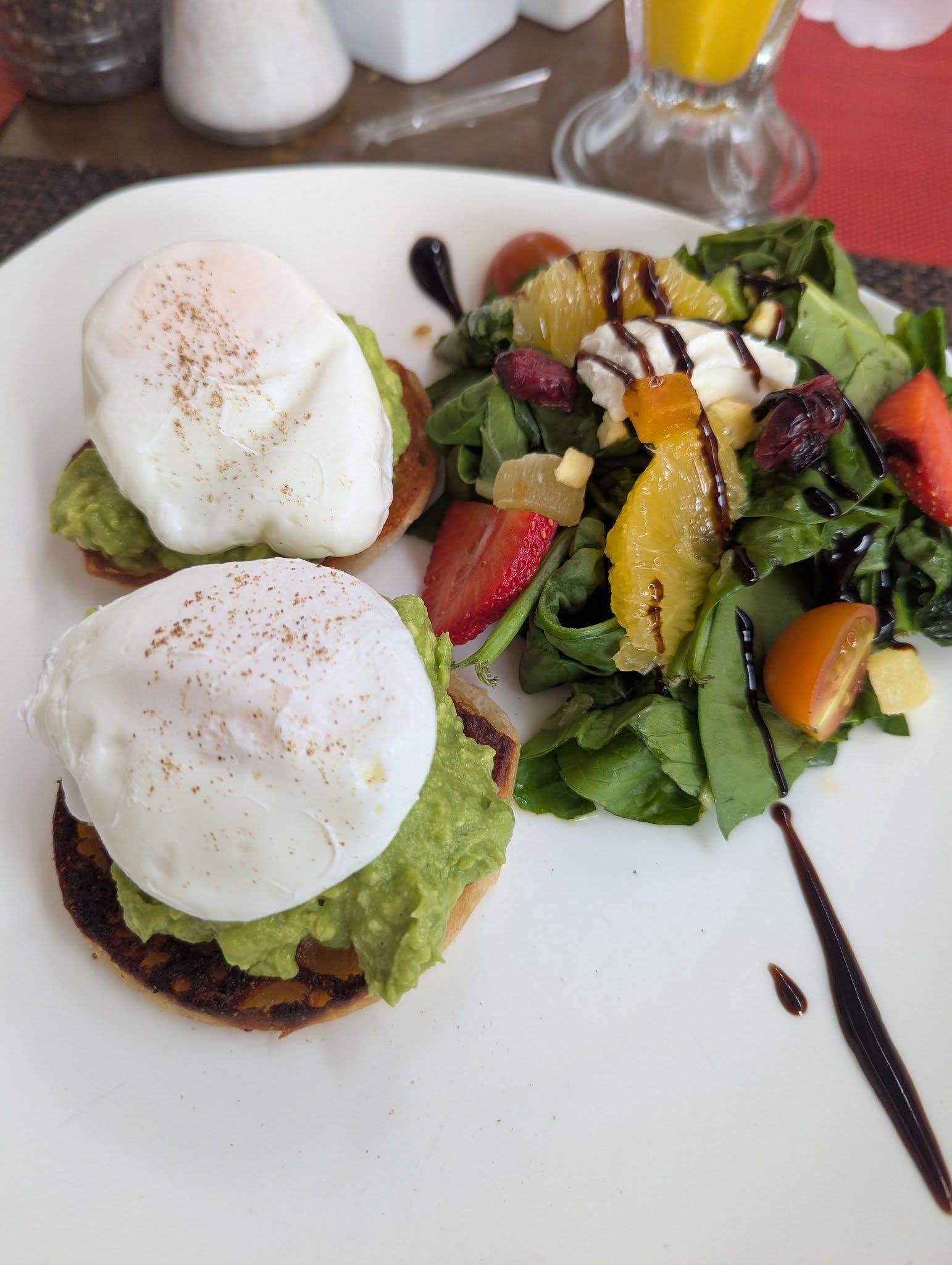 A white plate topped with avocado poached eggs and a salad