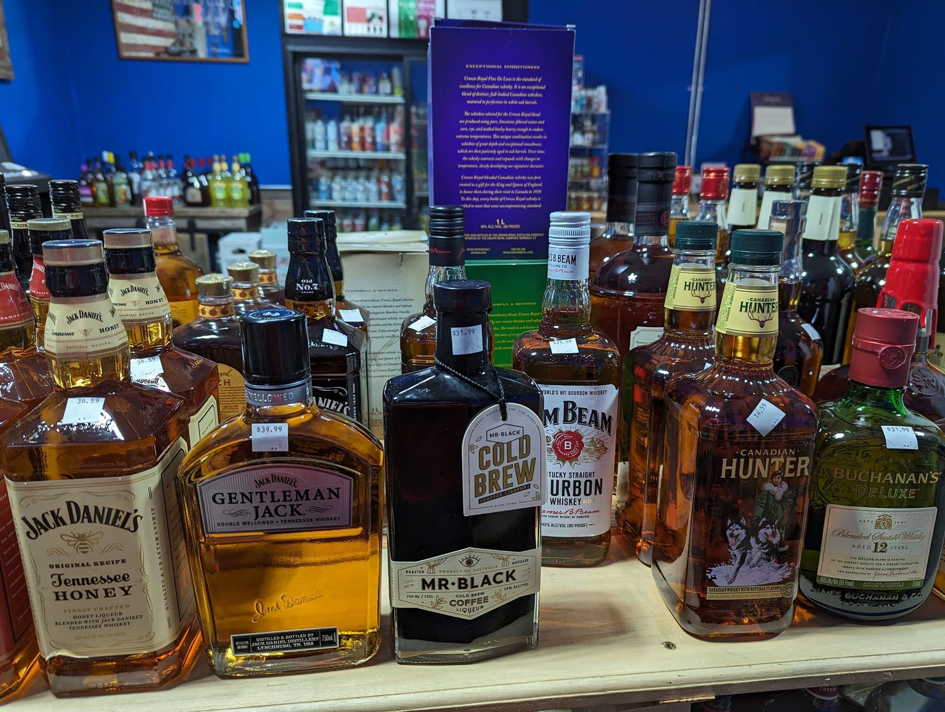Many bottles of alcohol are lined up on a shelf including jack daniels