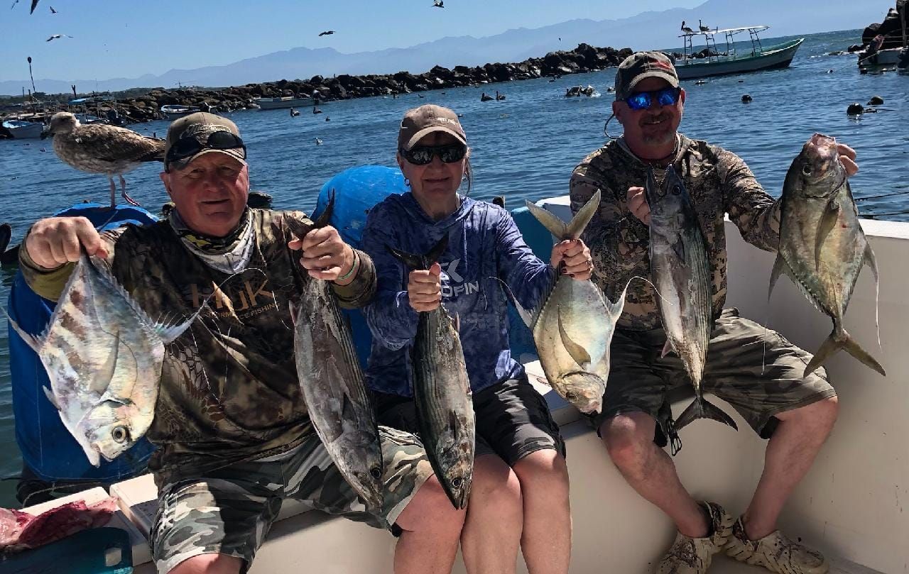 Three men are sitting on a boat holding fish.