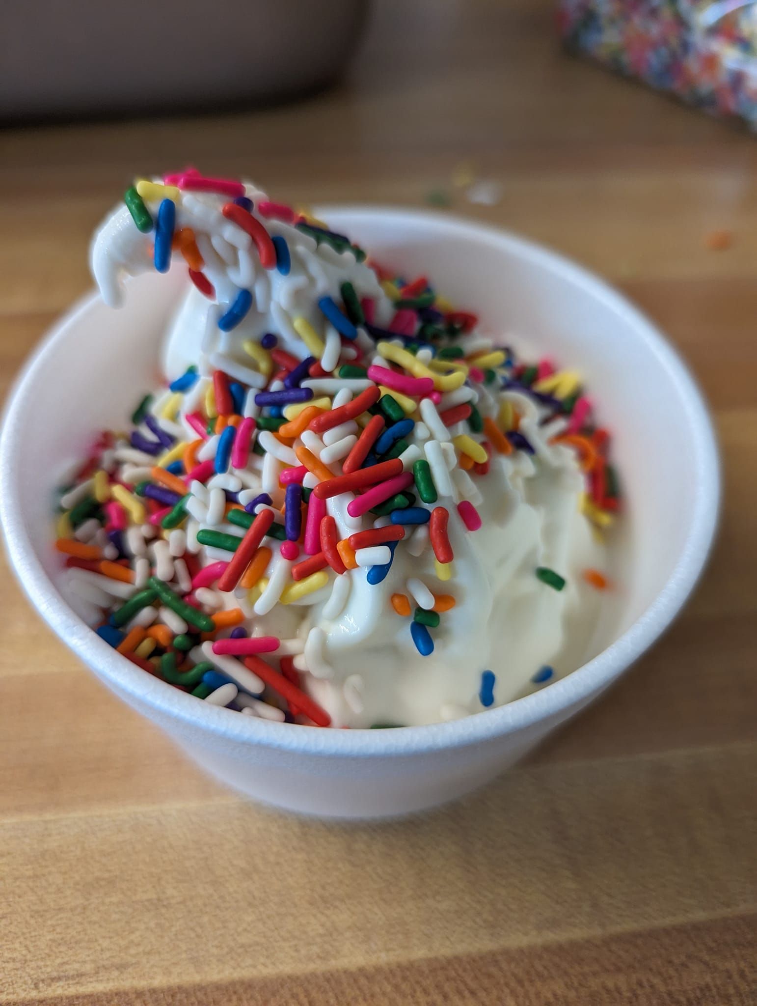 A bowl of ice cream with sprinkles on a wooden table.