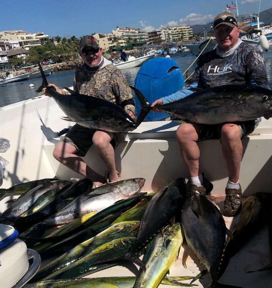 Two men are sitting on a boat holding large fish