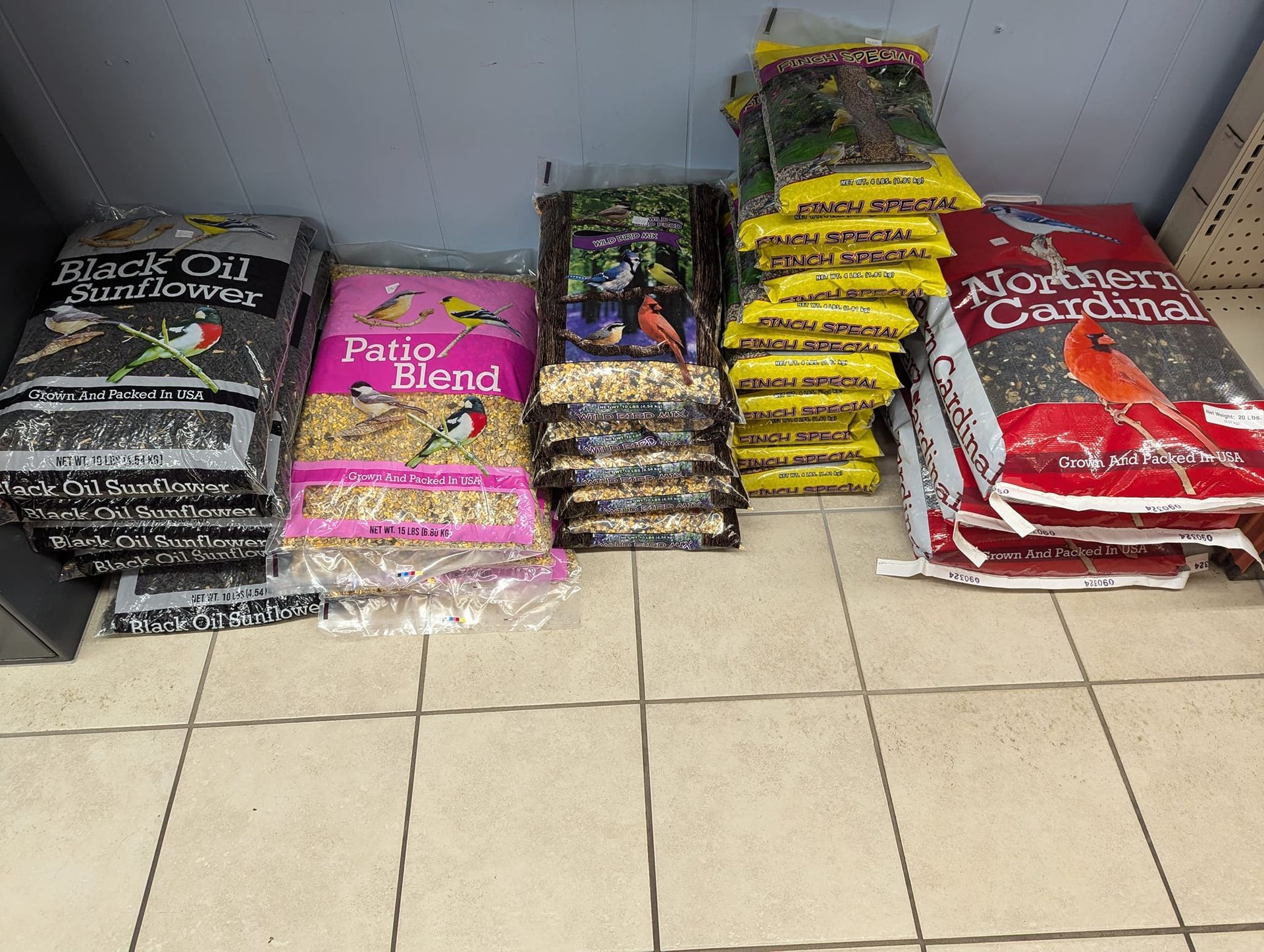 A bunch of bags of bird food are stacked on top of each other on a tiled floor.
