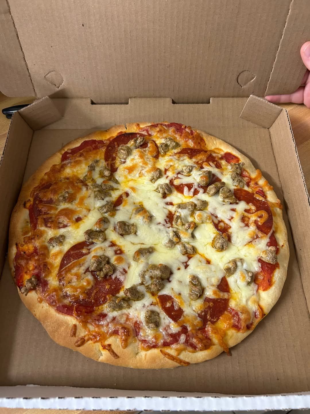 A pizza with pepperoni and sausage is in a cardboard box.