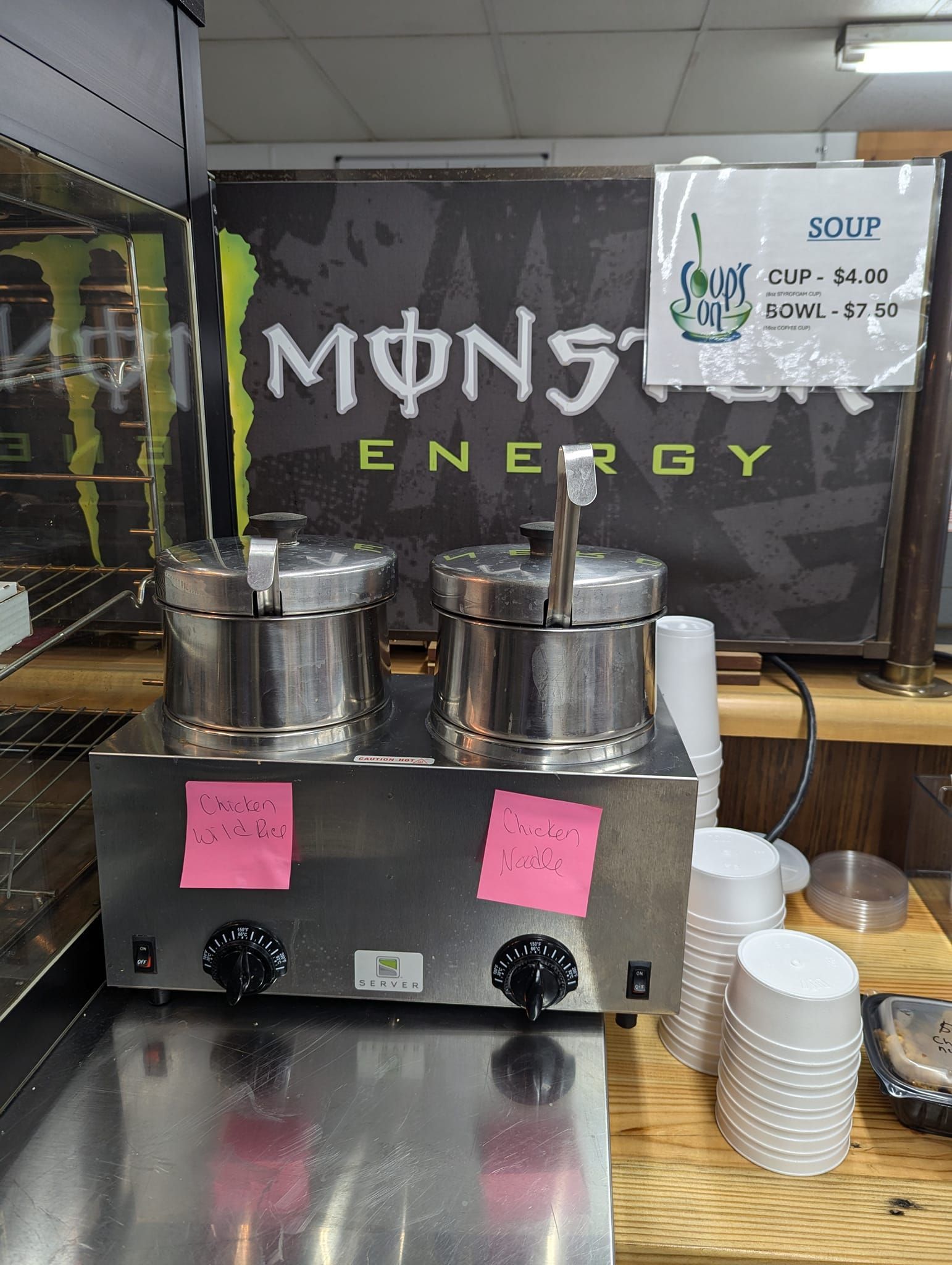 A stainless steel machine is sitting on a counter in front of a monster energy sign.
