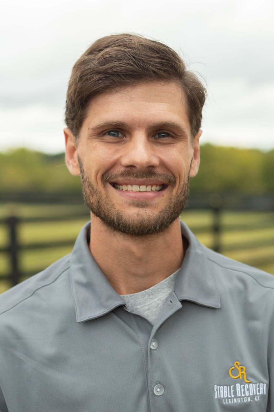 A man with a beard is wearing a baseball cap and a black shirt.