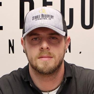 A man with a beard is wearing a baseball cap and a black shirt.