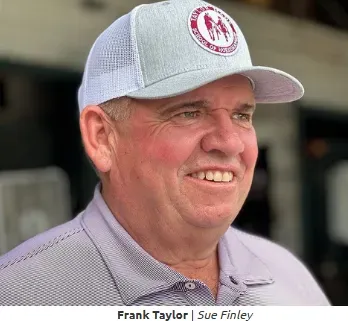 A man wearing a white hat and a purple shirt is smiling.