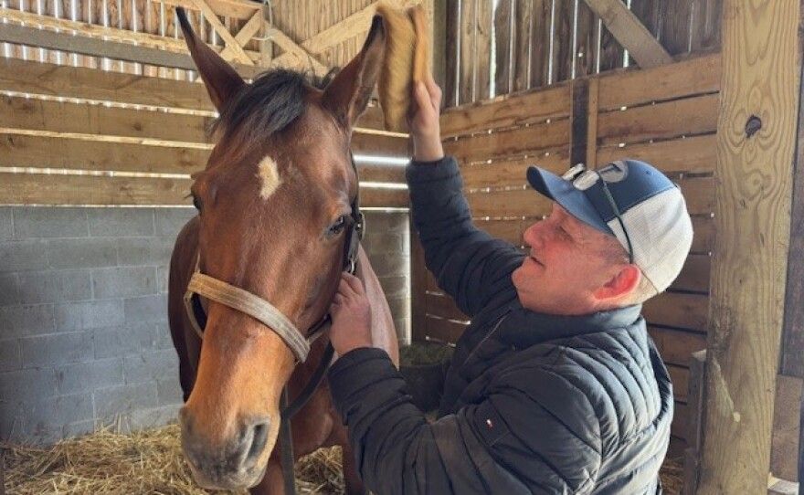 A man is petting a brown horse in a stable.