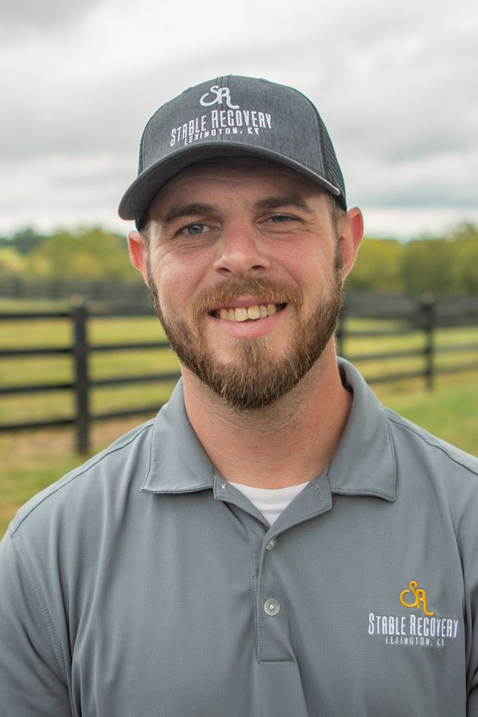 A man with a beard is wearing a baseball cap and a black shirt.