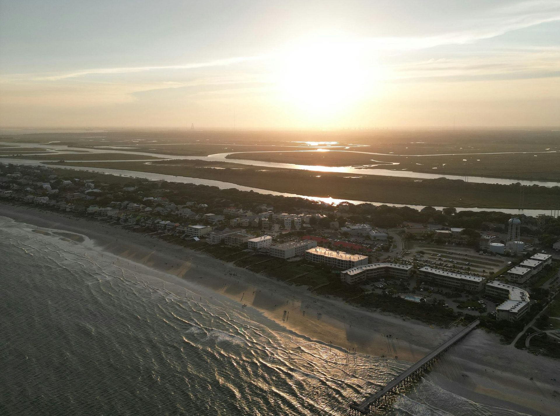 An aerial view of a beach at sunset with a pier in the foreground