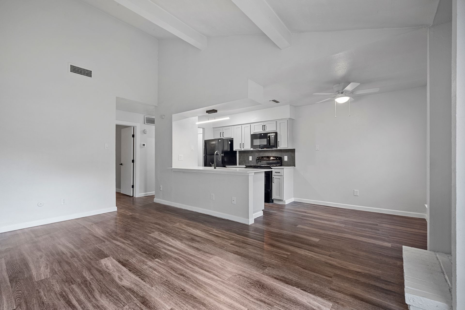 Photo showing a living room with the kitchen in the background and a dining area in the middleground