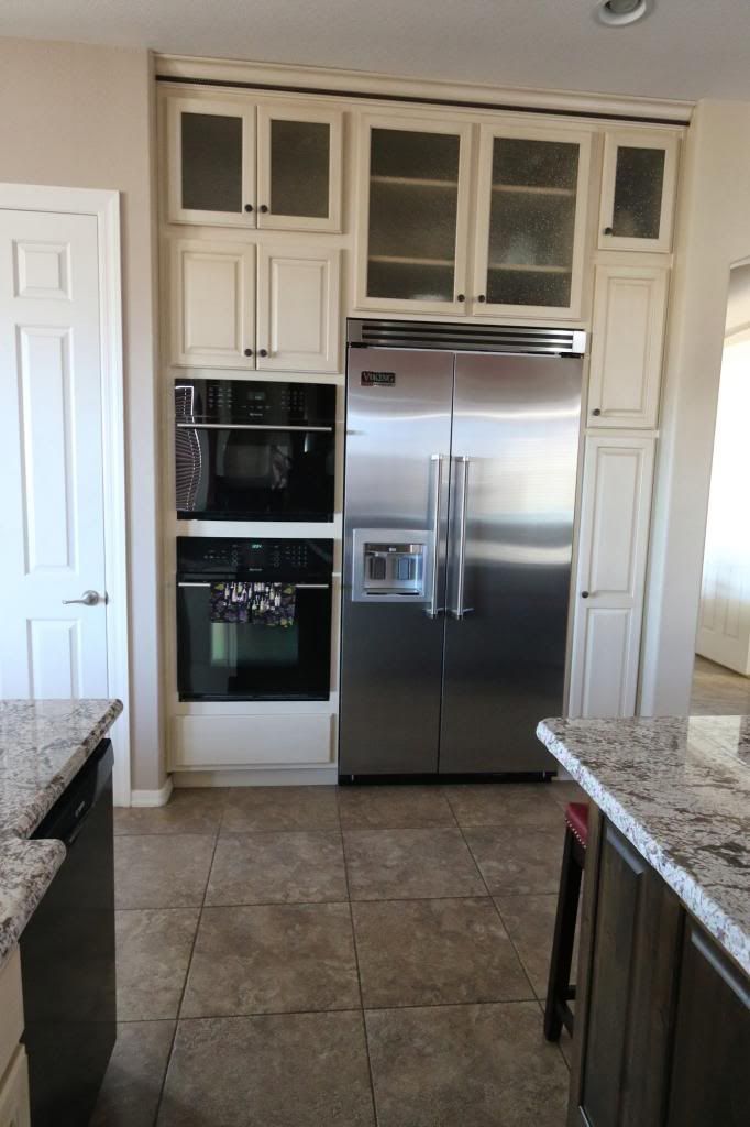 Kitchen with off-white cabinets, stainless steel refrigerator, and built-in ovens. Tile floor and granite countertops.