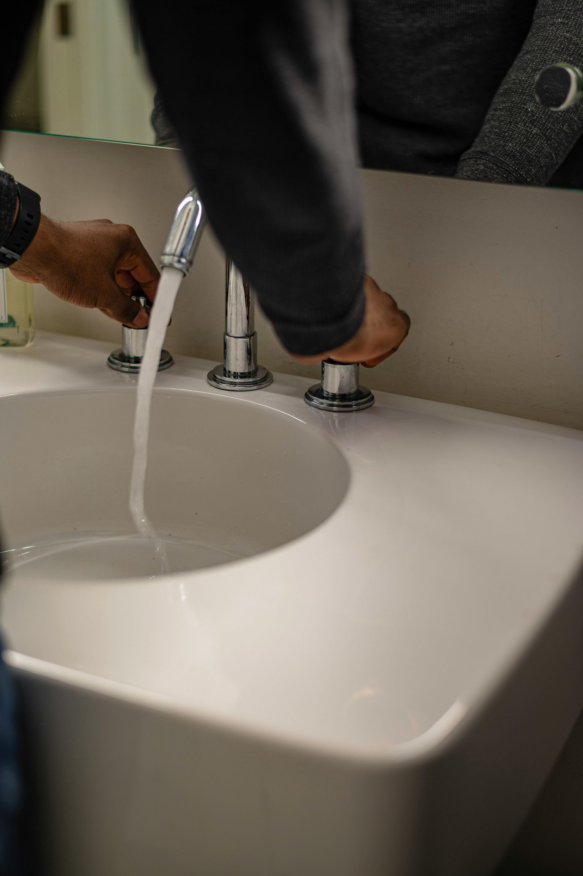 Person turning on a bathroom sink faucet with running water.