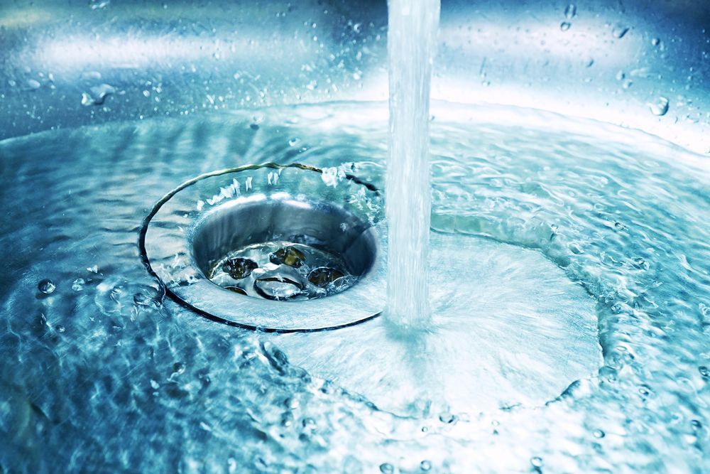 Close-up of water pouring into a stainless steel sink drain, creating ripples and splashes.