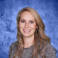A woman is smiling for a picture in front of a blue background.