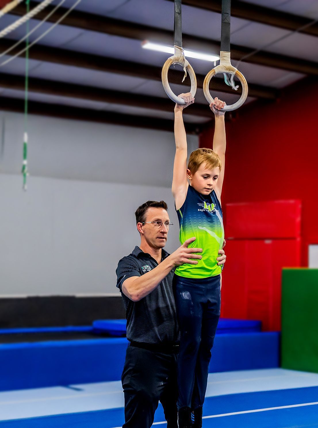 A man is helping a young boy do gymnastics on rings.