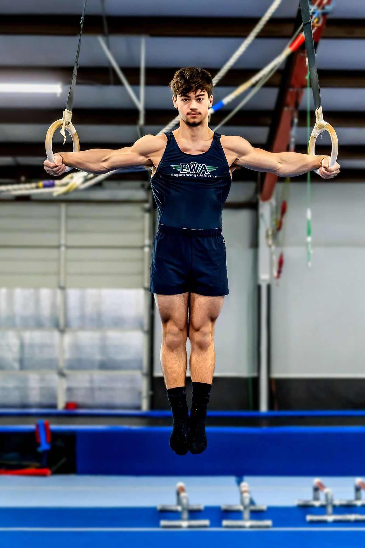 A young man is doing gymnastics on rings in a gym.