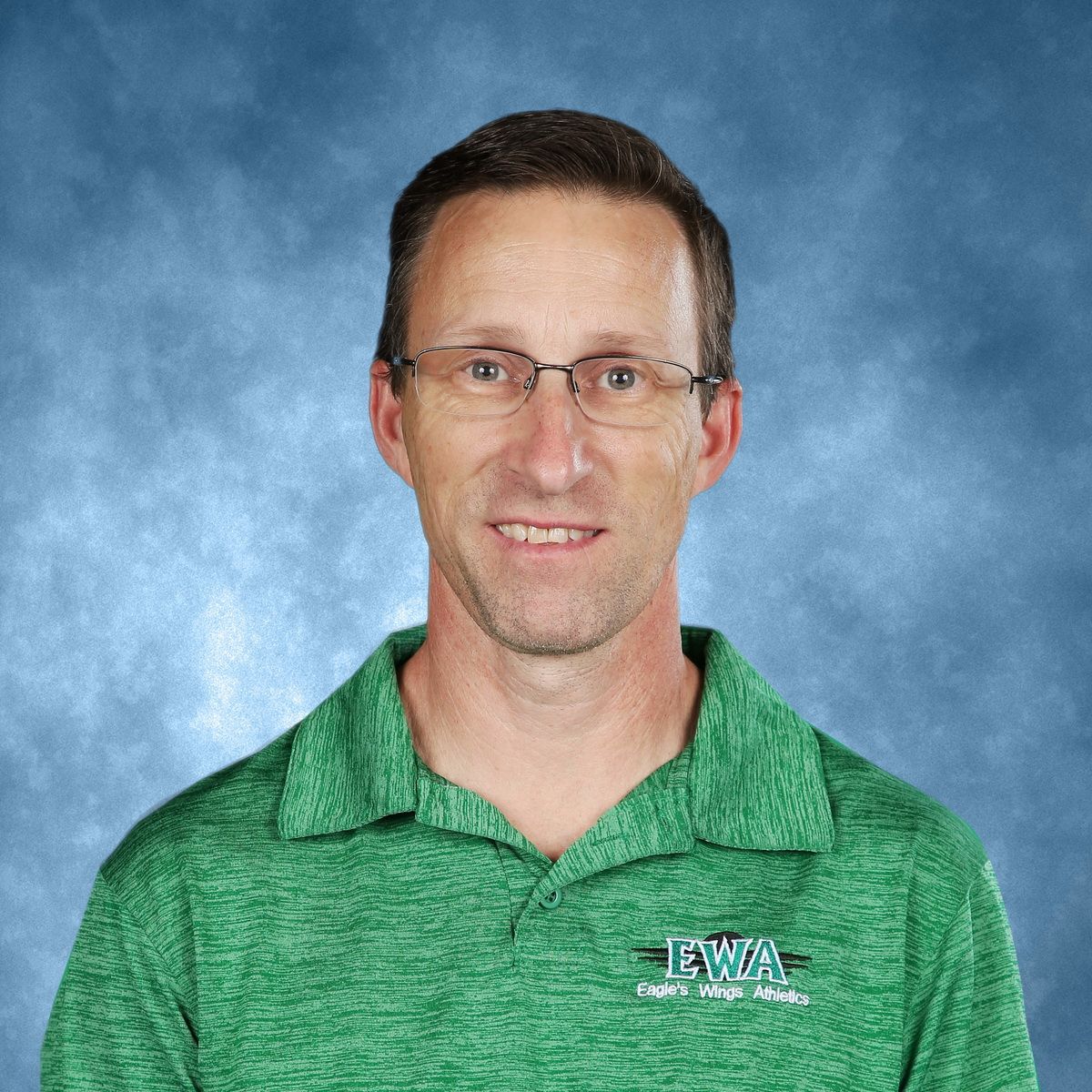 A man in a blue shirt is smiling with his arms crossed.