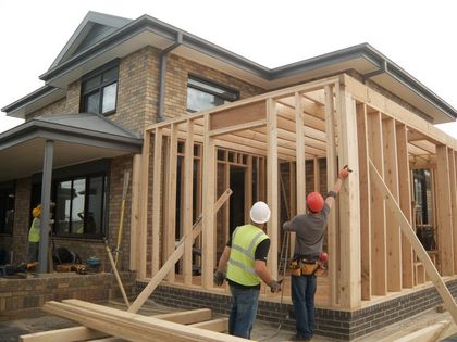 Construction workers building a wooden frame extension onto a brick home.