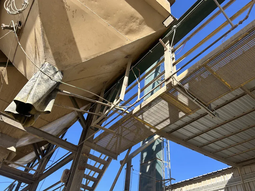 A complex industrial structure with metal walkways and staircases, viewed from below against a blue sky.