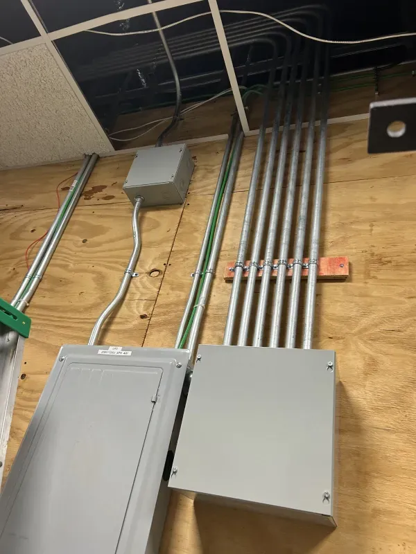Electrical wiring on a wooden wall with metal conduits, boxes, and a breaker panel.