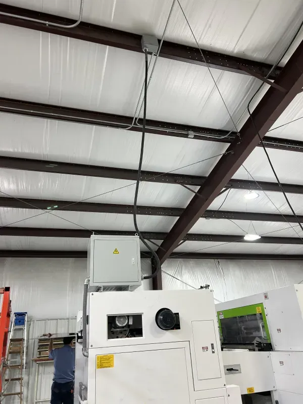 Electrical conduit and boxes on a ceiling, powering a large white industrial machine.