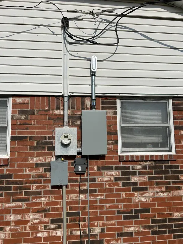 Electrical equipment mounted on a brick wall, including a meter box, conduit, and gray panel.
