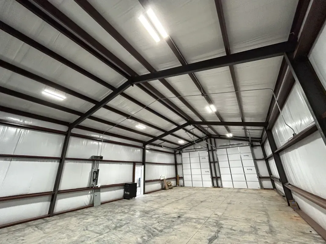 Interior of an empty metal warehouse with insulation and overhead lights.