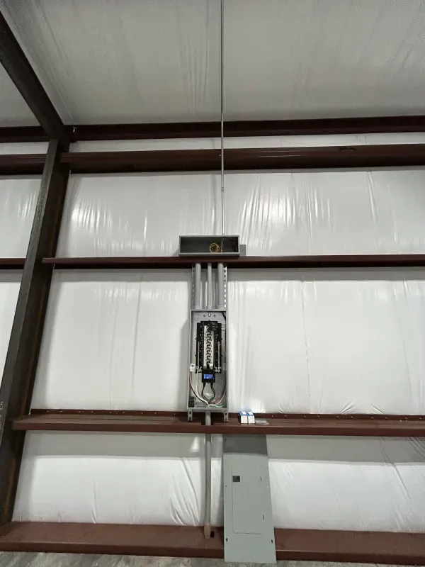 Electrical panel and conduit mounted on white insulated wall of a metal-framed building.