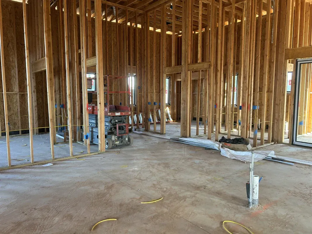 Interior view of a house under construction, showing wooden framing, concrete floor, and electrical wiring.