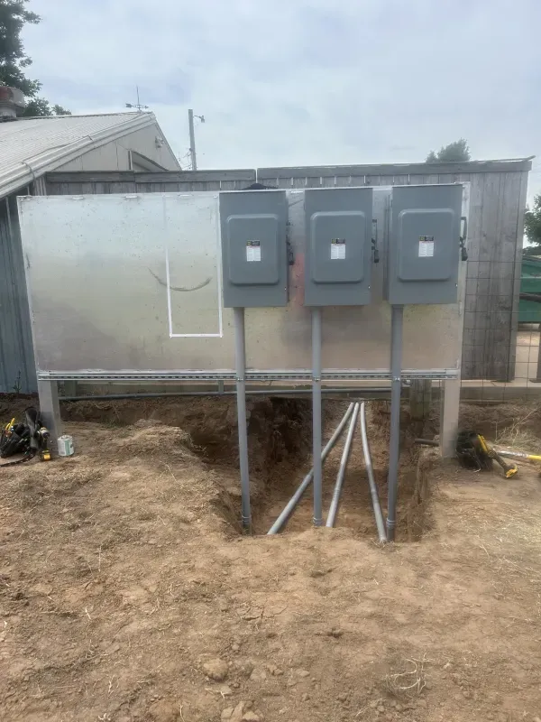 Three gray electrical boxes mounted on metal poles outside a building in a dirt yard.