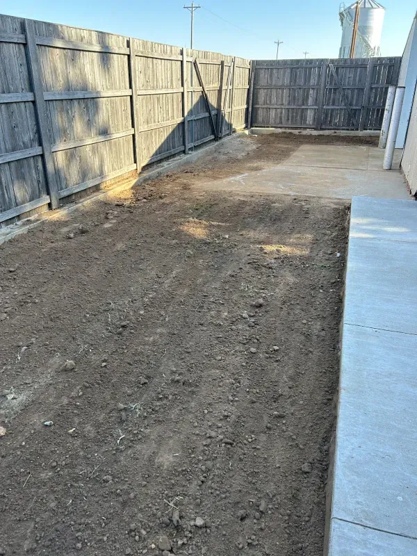 Dirt backyard with wooden fence on two sides. Concrete patio on right.