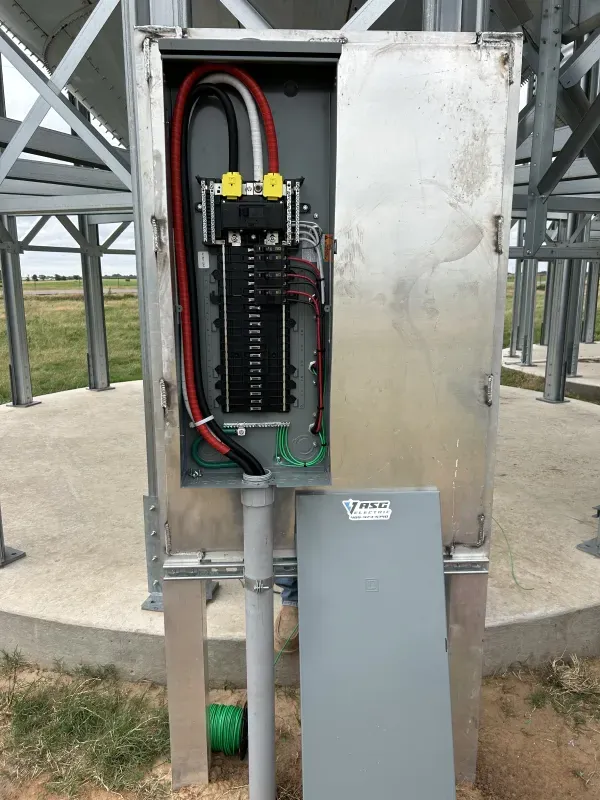 Electrical panel box on a concrete base with wires and conduit, outdoors.
