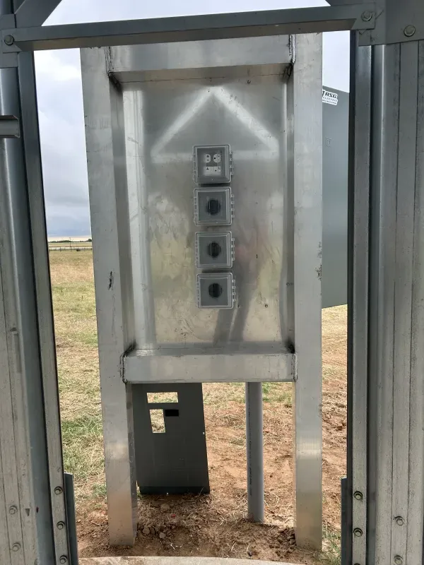 Metal gate with four buttons on a control panel, set against a field.
