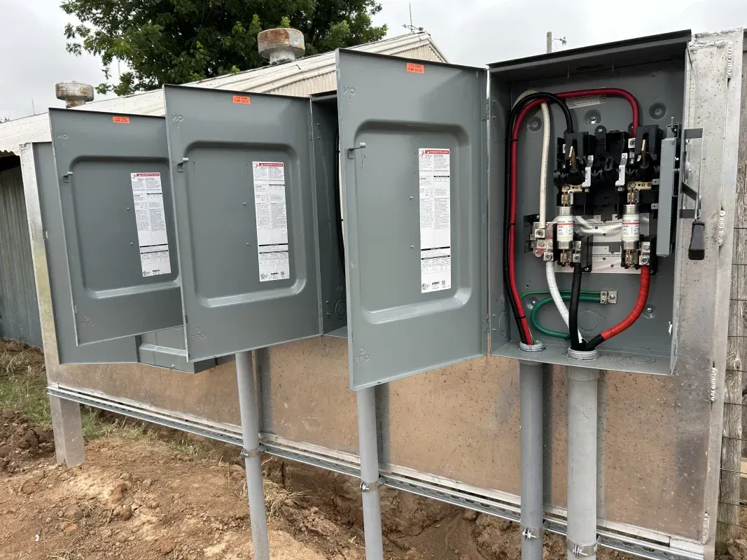 Outdoor electrical panel with three gray metal boxes on pedestals. One box is open, revealing wires.