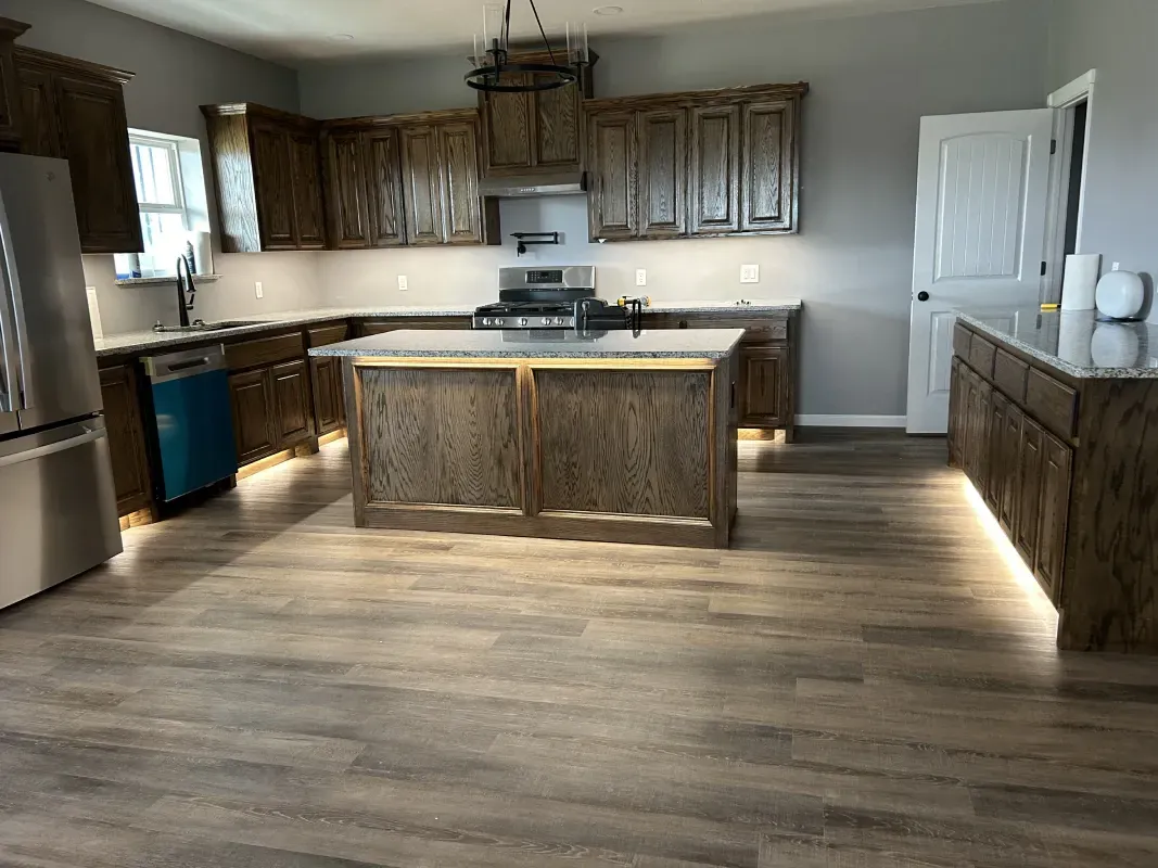 Kitchen with brown cabinets, island, stainless steel appliances, and wood flooring.