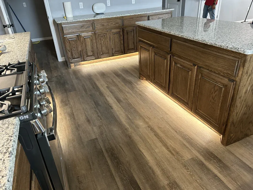 Kitchen with wood cabinets, granite countertops, and under-cabinet lighting; light wood flooring.