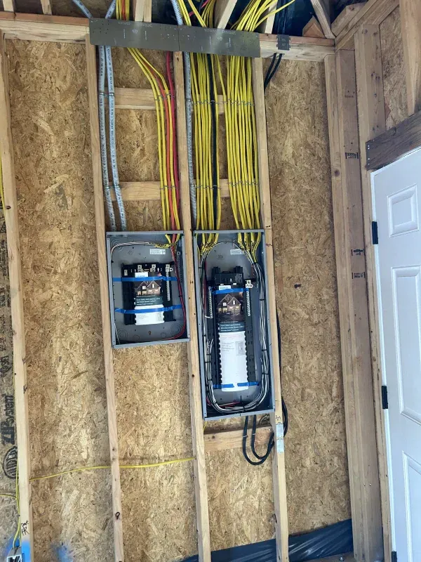 Two electrical panels mounted on a wood-framed wall; yellow wires feed into them from above.