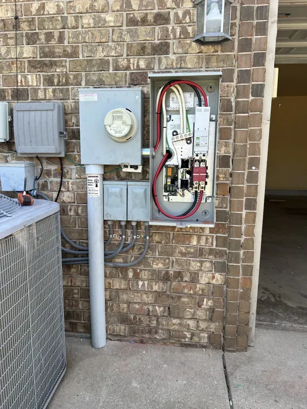 Outdoor electrical panel on a brick wall, with conduit and wires visible.