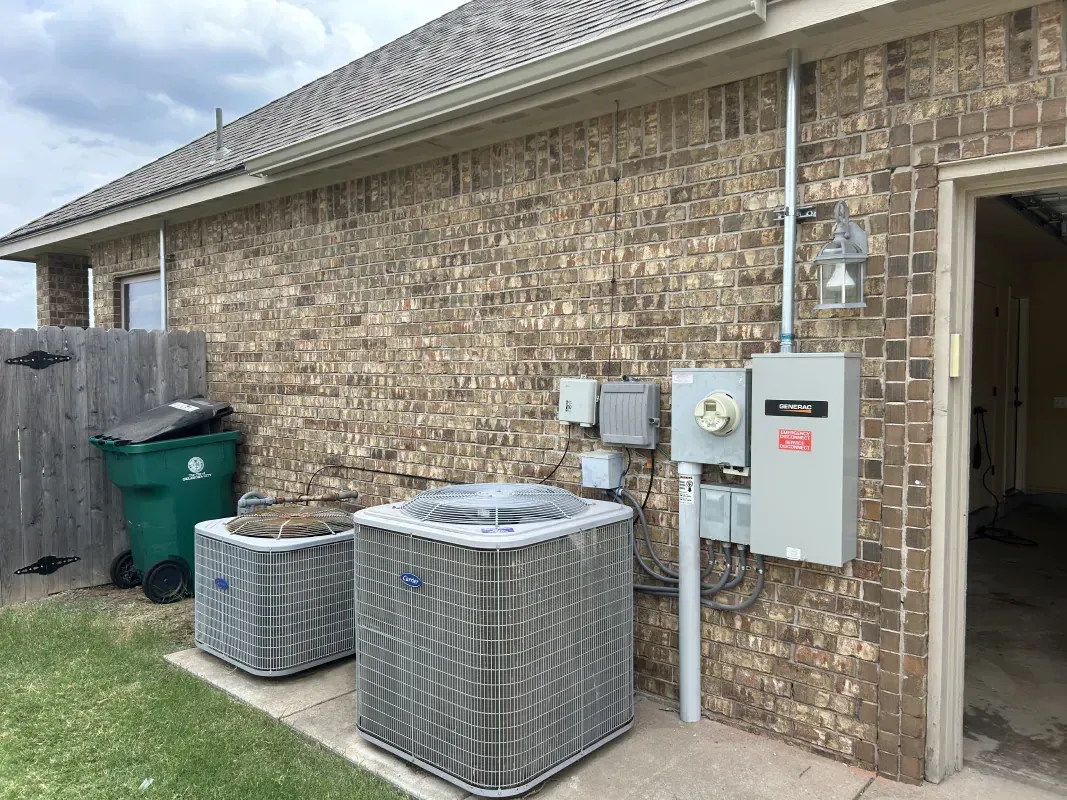 Two AC units next to a brick building with electrical components. A green trash bin is nearby.
