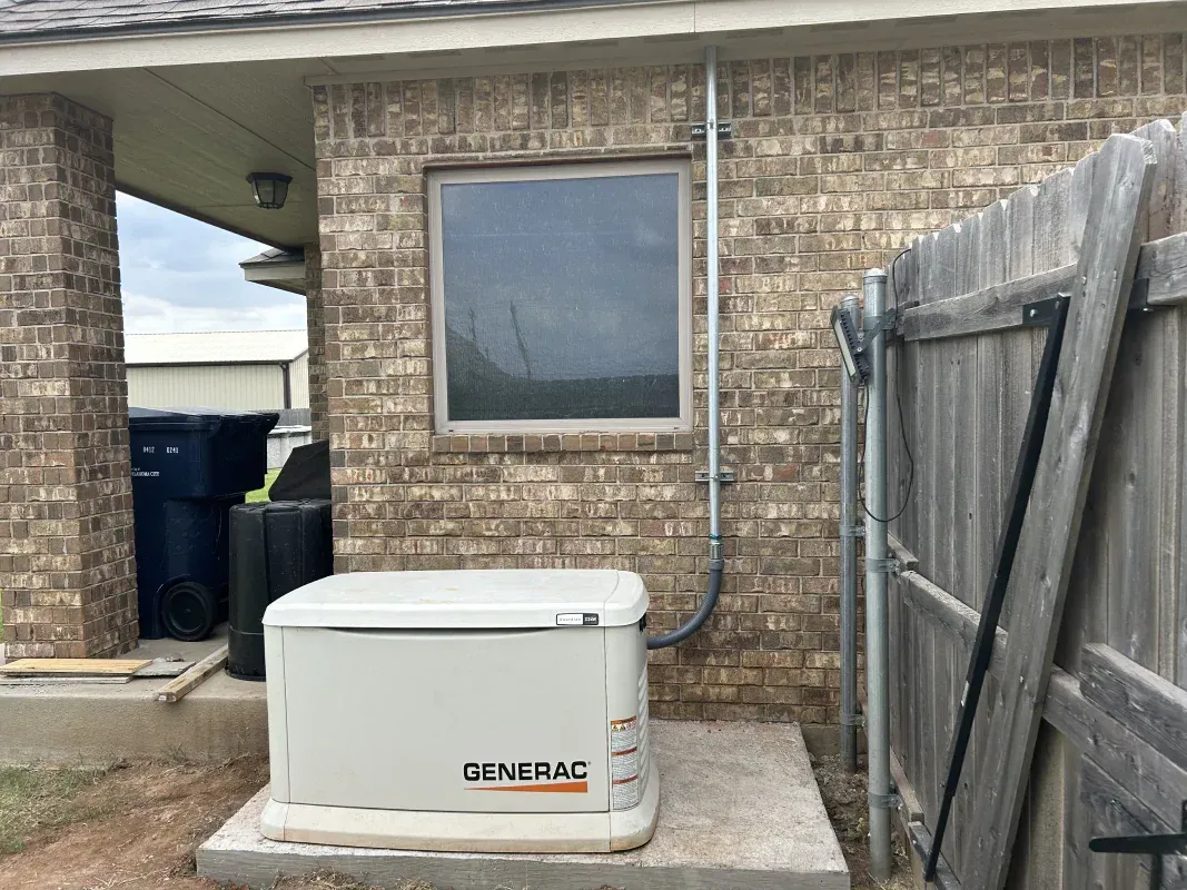 A Generac home generator sits on a concrete pad next to a brick wall and window.