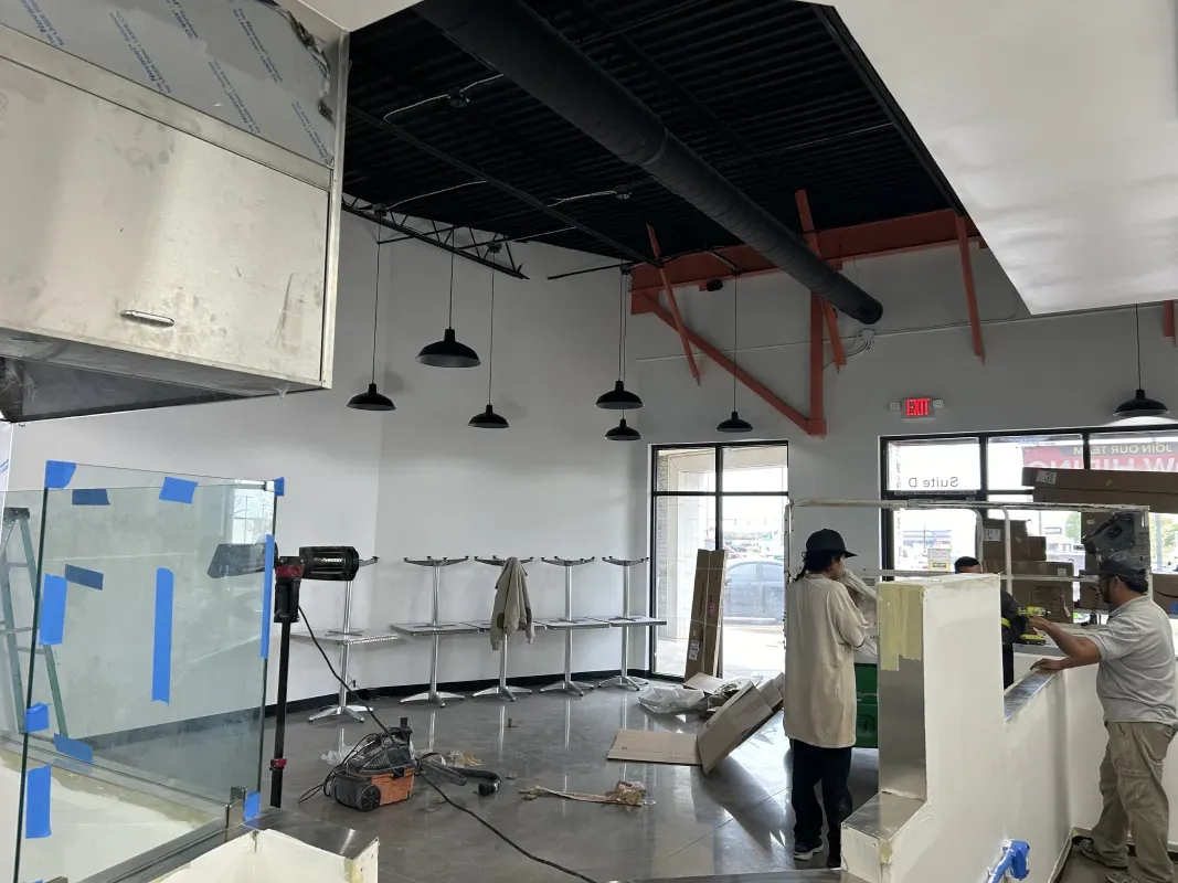 Interior construction: Workers and equipment in a bright, open space. Black ceiling, white walls, and various metal fixtures.